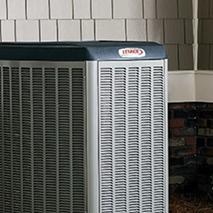 An outdoor Lennox air conditioning unit installed near a house wall with beige siding and a small section of brickwork. An outdoor Lennox air conditioning unit installed near a house wall with beige siding and a small section of brickwork.