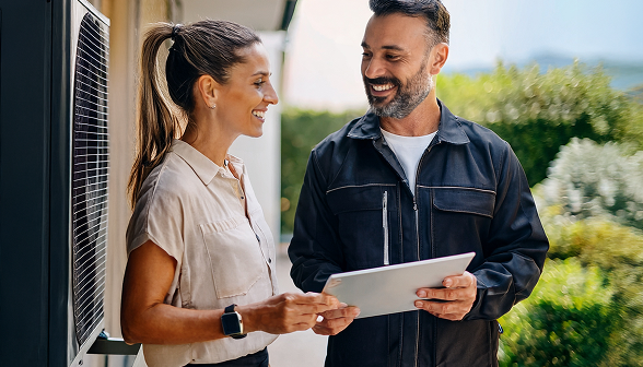 A Bosanac specialist and a smiling client stand beside an outdoor HVAC unit, reviewing information on a tablet together. A Bosanac specialist and a smiling client stand beside an outdoor HVAC unit, reviewing information on a tablet together.
