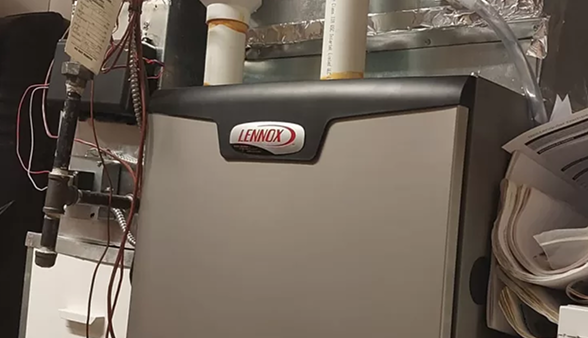 A Lennox heating system unit with connected pipes and electrical wiring installed indoors, surrounded by papers and metallic ductwork. A Lennox heating system unit with connected pipes and electrical wiring installed indoors, surrounded by papers and metallic ductwork.