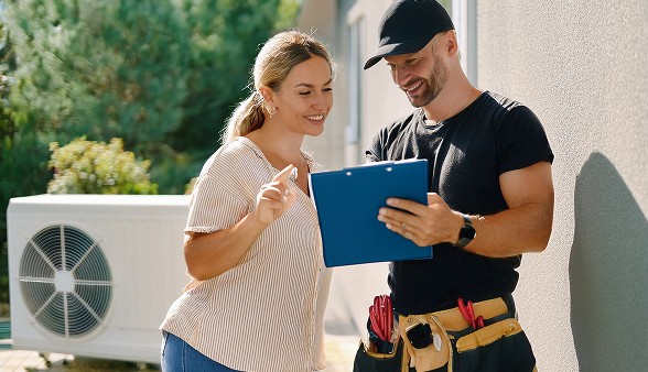 A Bosanac technician discusses financing options with a homeowner while standing next to an outdoor HVAC unit. A Bosanac technician discusses financing options with a homeowner while standing next to an outdoor HVAC unit.